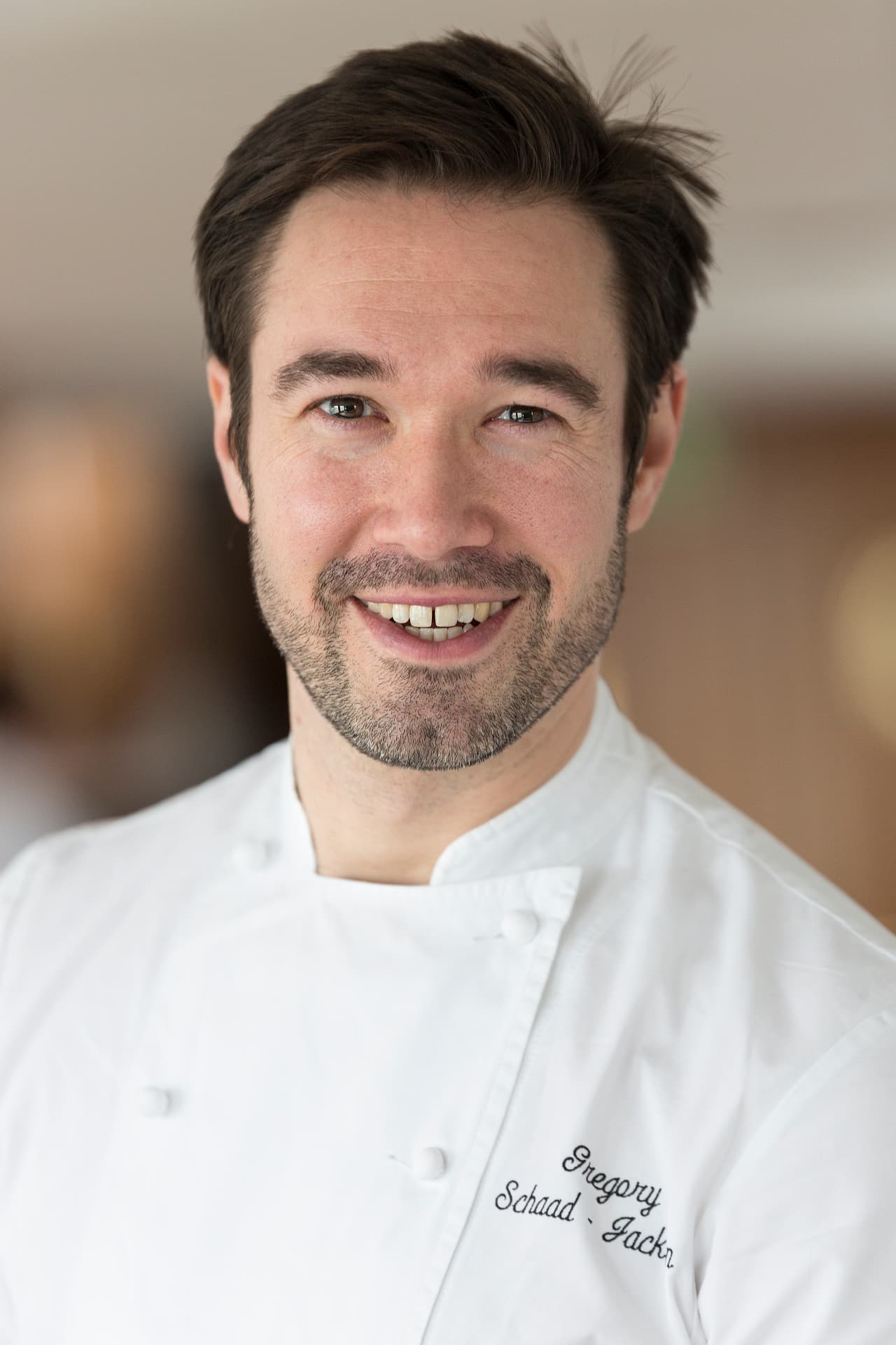 Close portrait of Gregory smiling in an embroidered chef jacket.