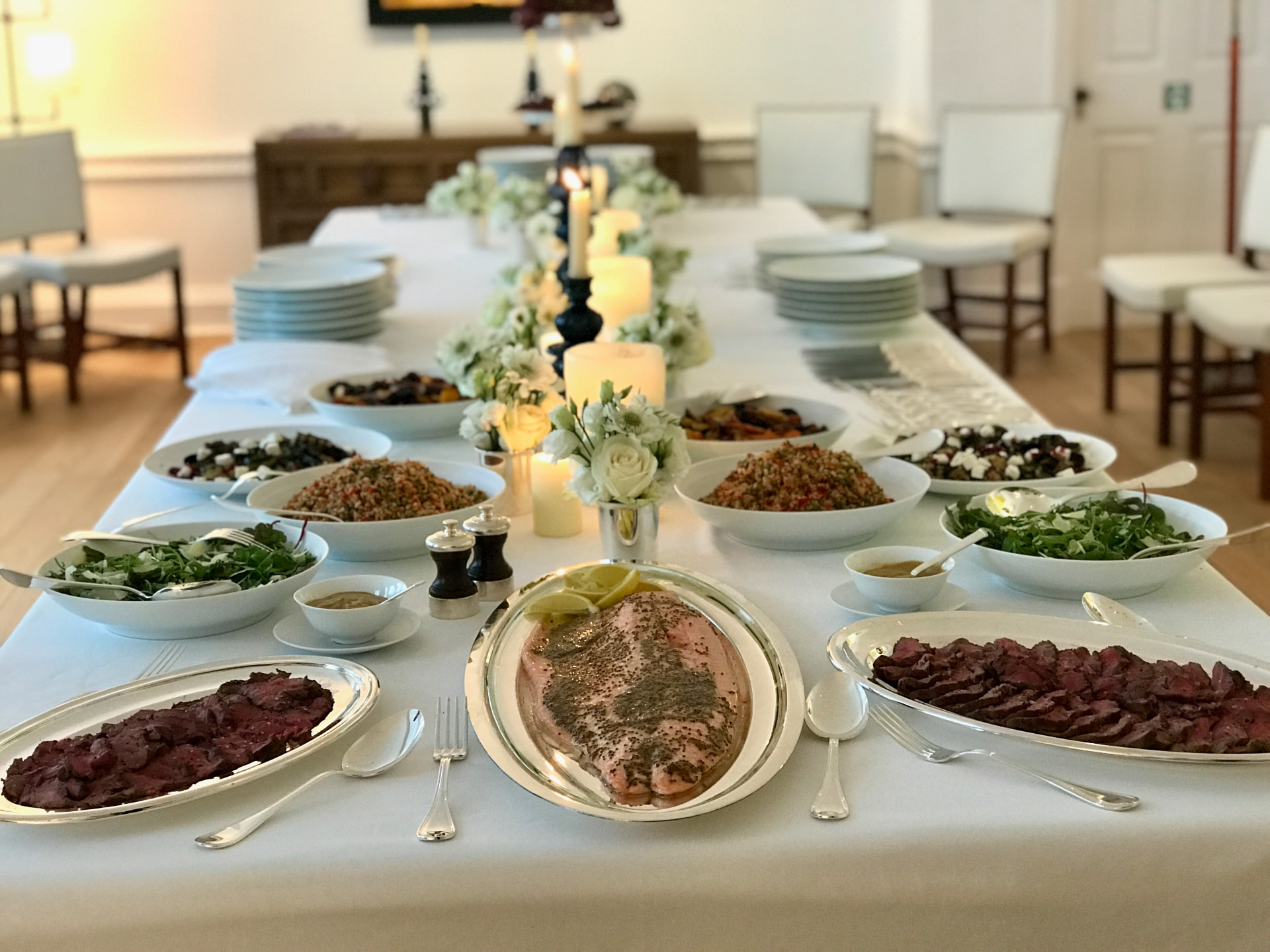 A candlelit table laid with salmon, salads and sliced roast beef.