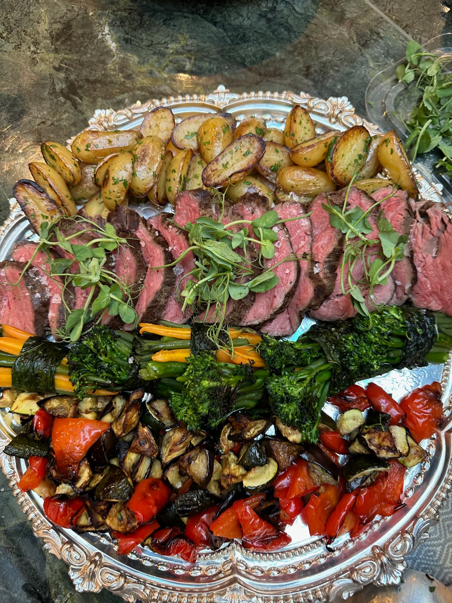Sliced beef, roast potatoes and vegetables on a silver platter.