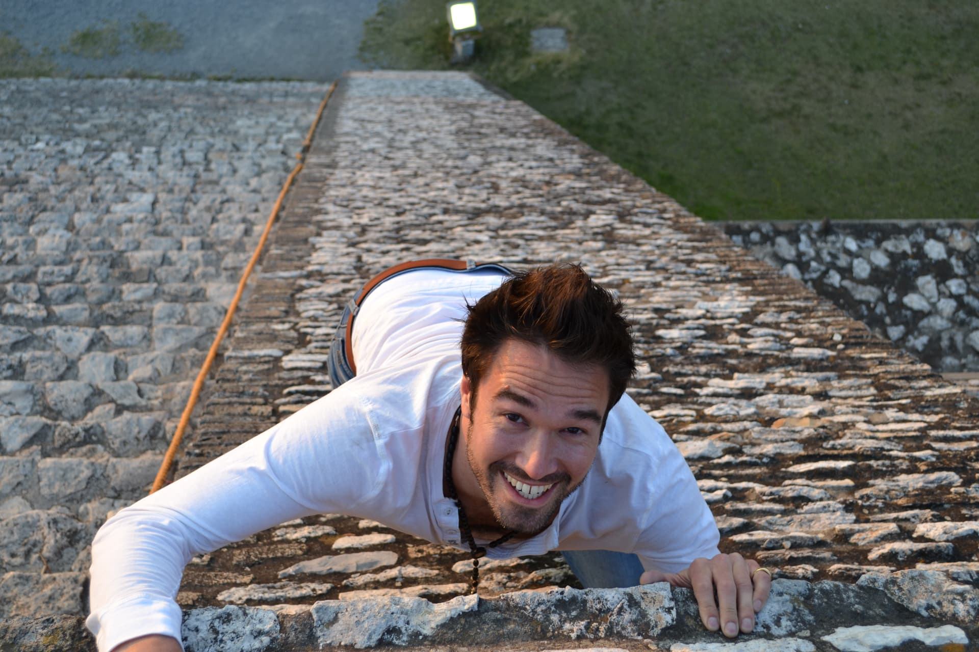 Gregory grinning as he climbs a steep stone pyramid.