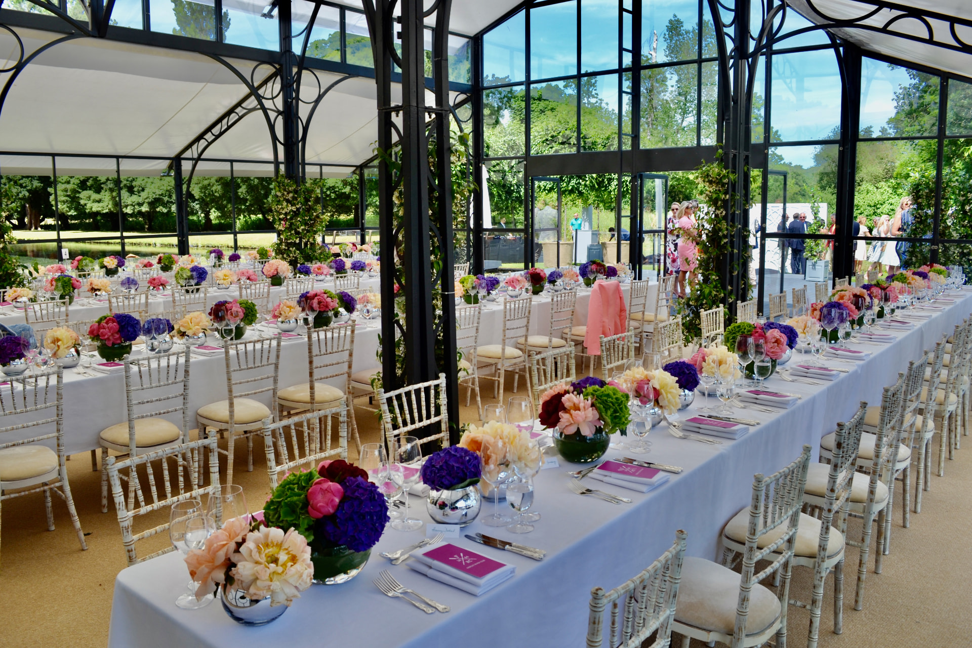 Long dining tables with colourful flowers in a glass pavilion.