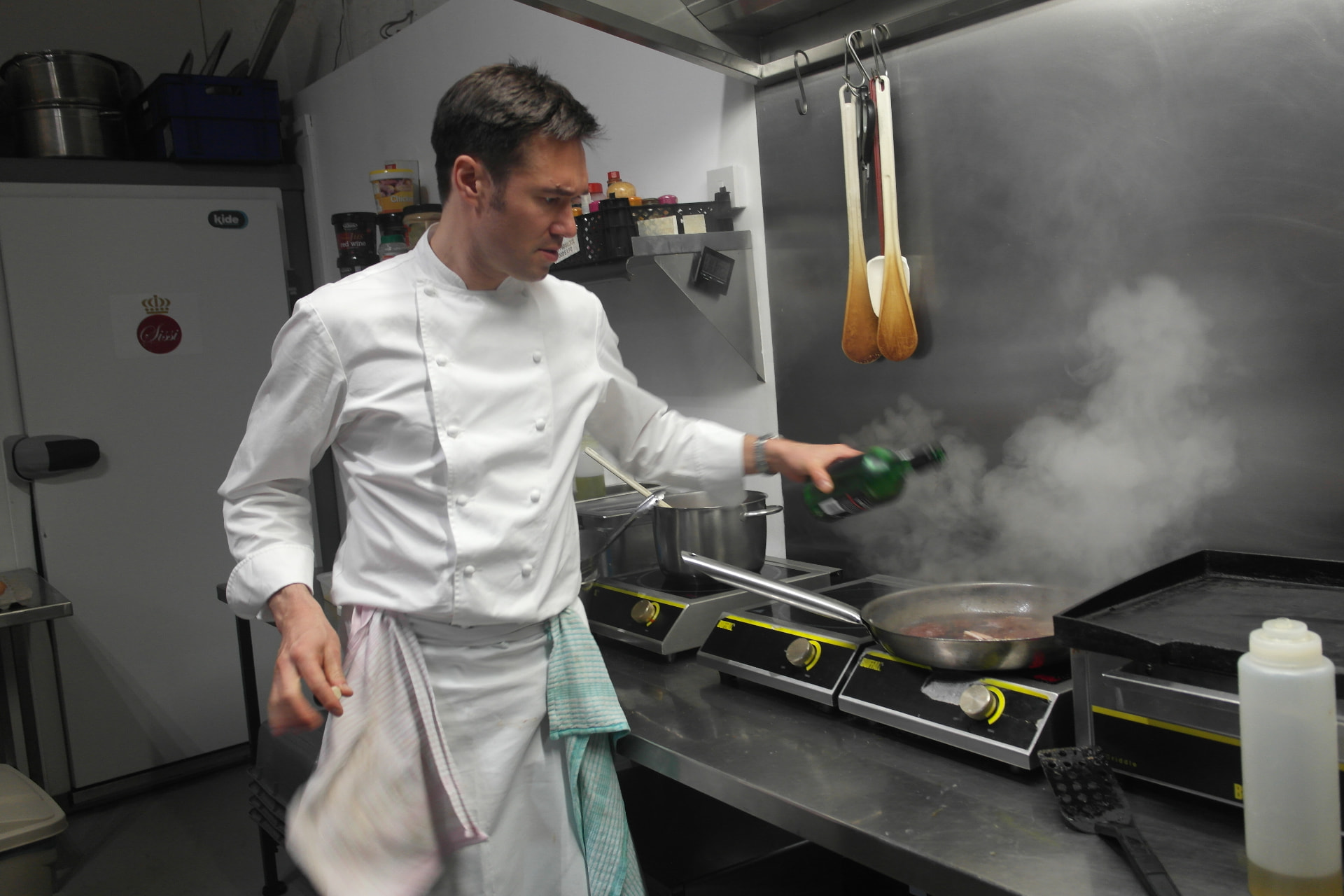 Gregory in chef whites deglazing a pan in a cloud of steam.