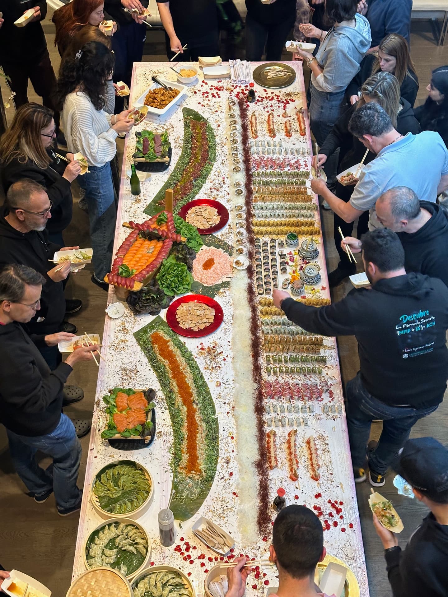 Guests gathered around the full length of an abundant sushi table.