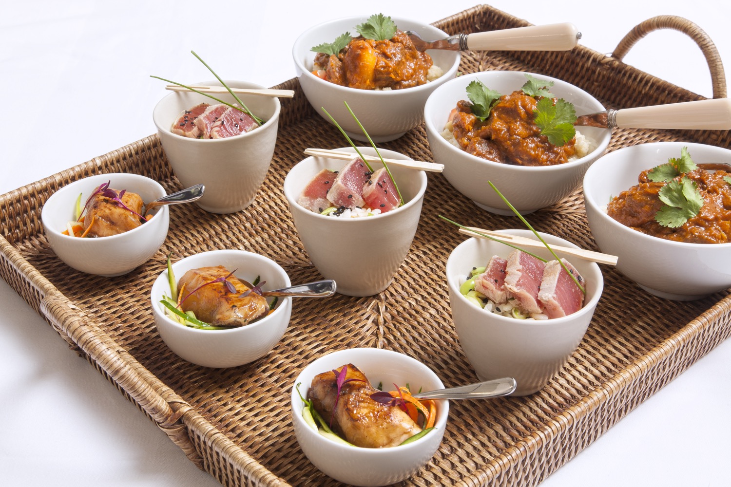 A wicker tray of small, colourful bowls of food.