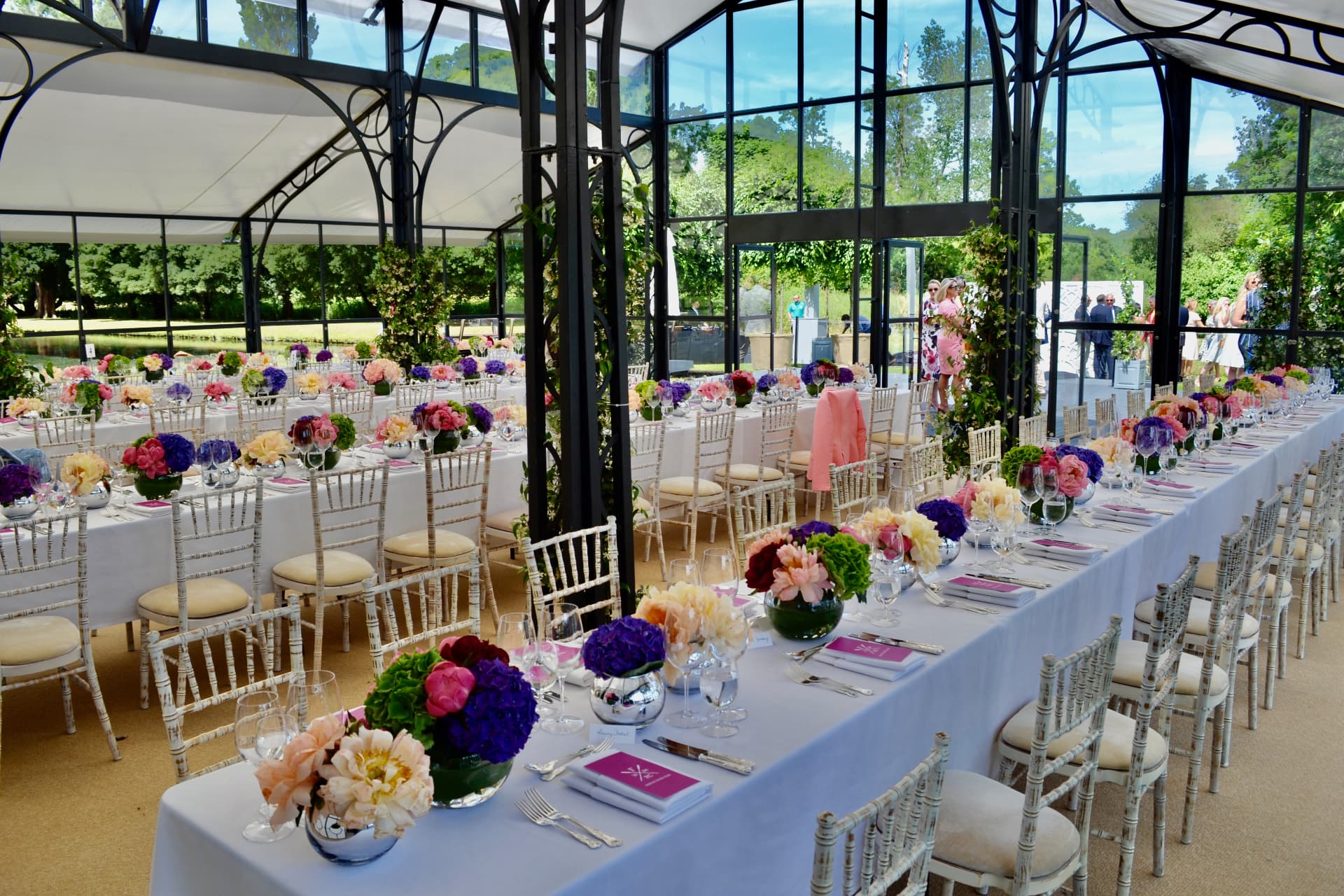 Long banqueting tables laid with flowers and glassware in a garden pavilion.