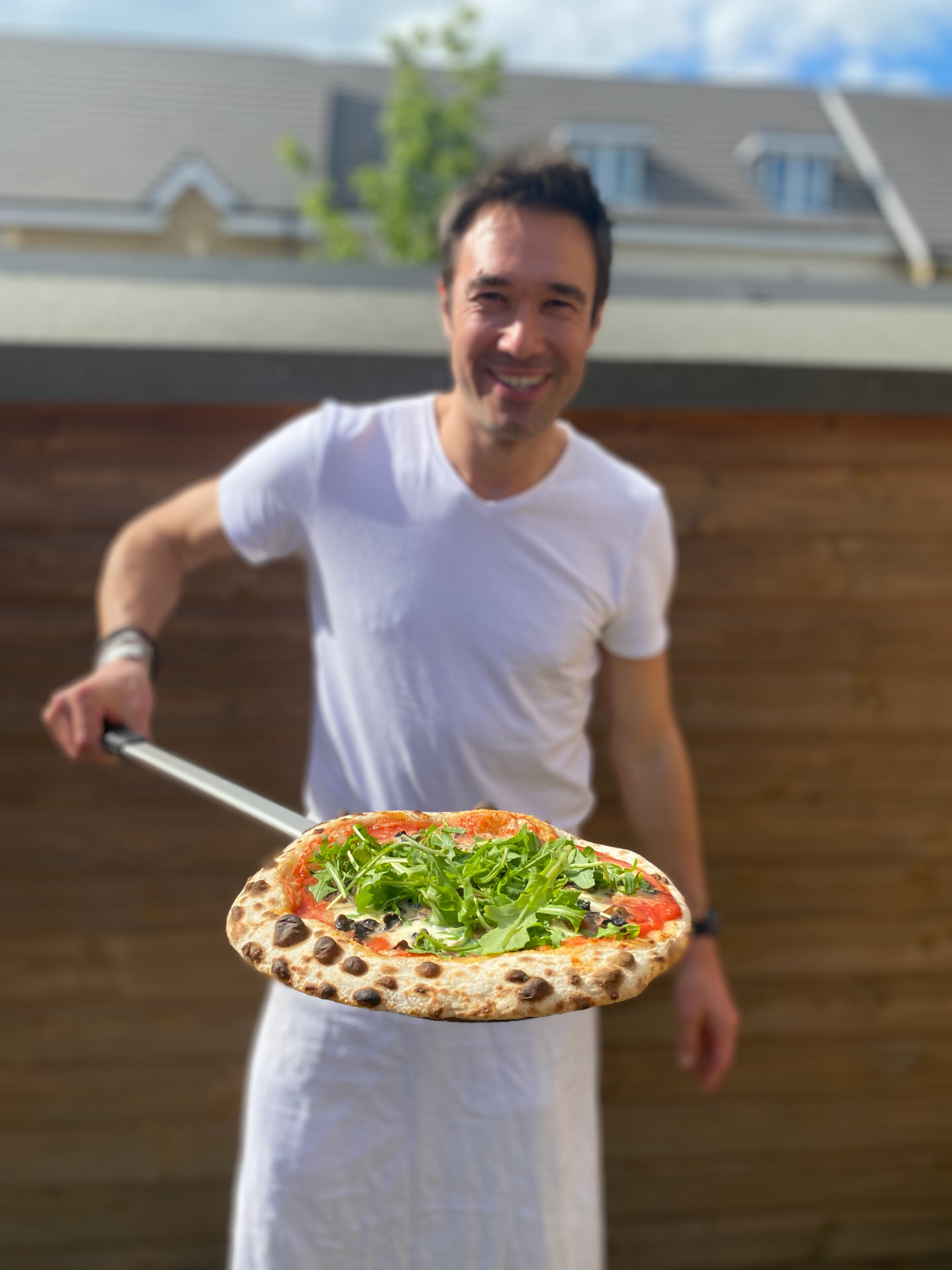 Gregory holding out a freshly baked pizza on a peel.