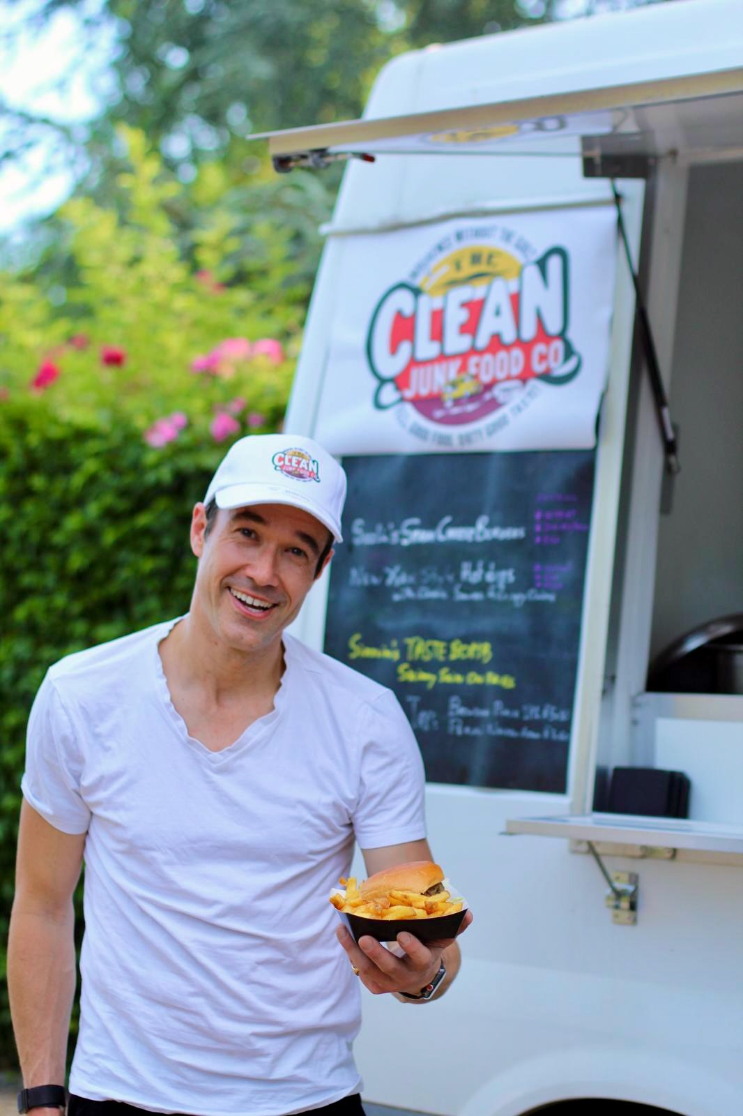 Gregory outside the Clean Junk Food Co. truck holding a burger and fries.