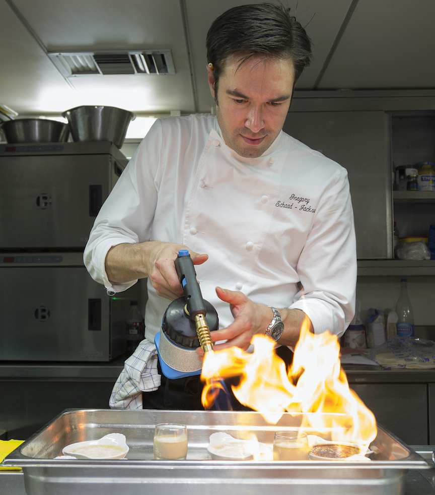 Gregory finishing a tray of food with a blowtorch, flame catching in the foreground.