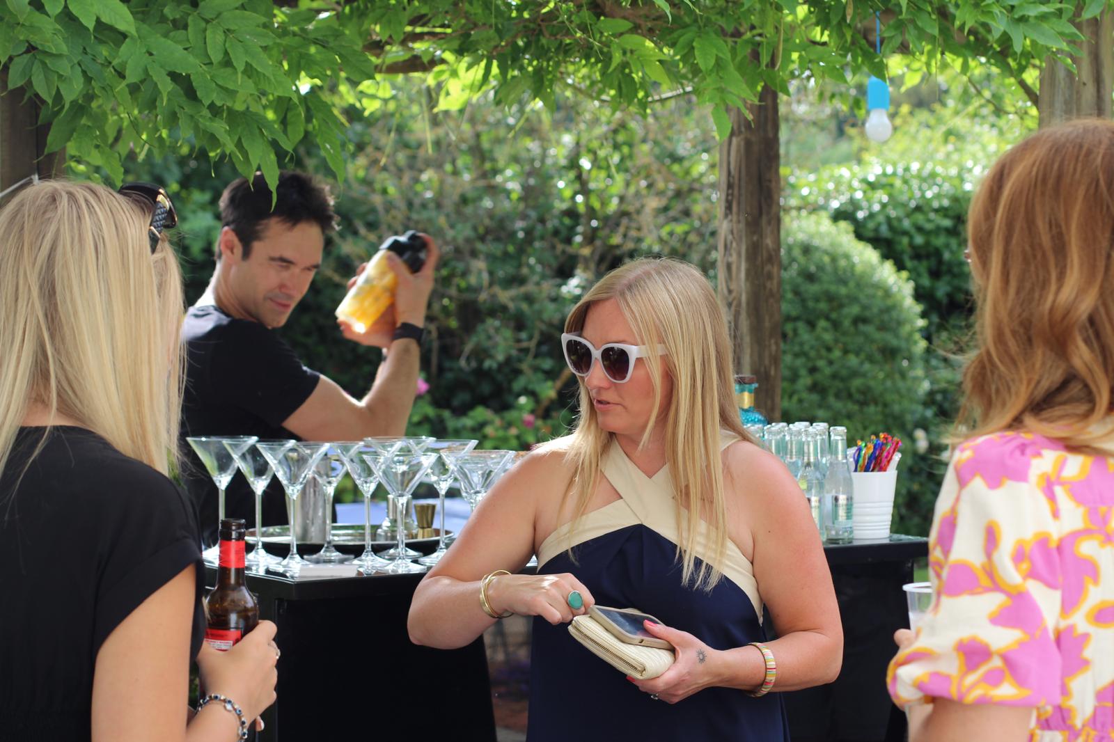 Guests talking beside an outdoor cocktail bar while drinks are shaken.