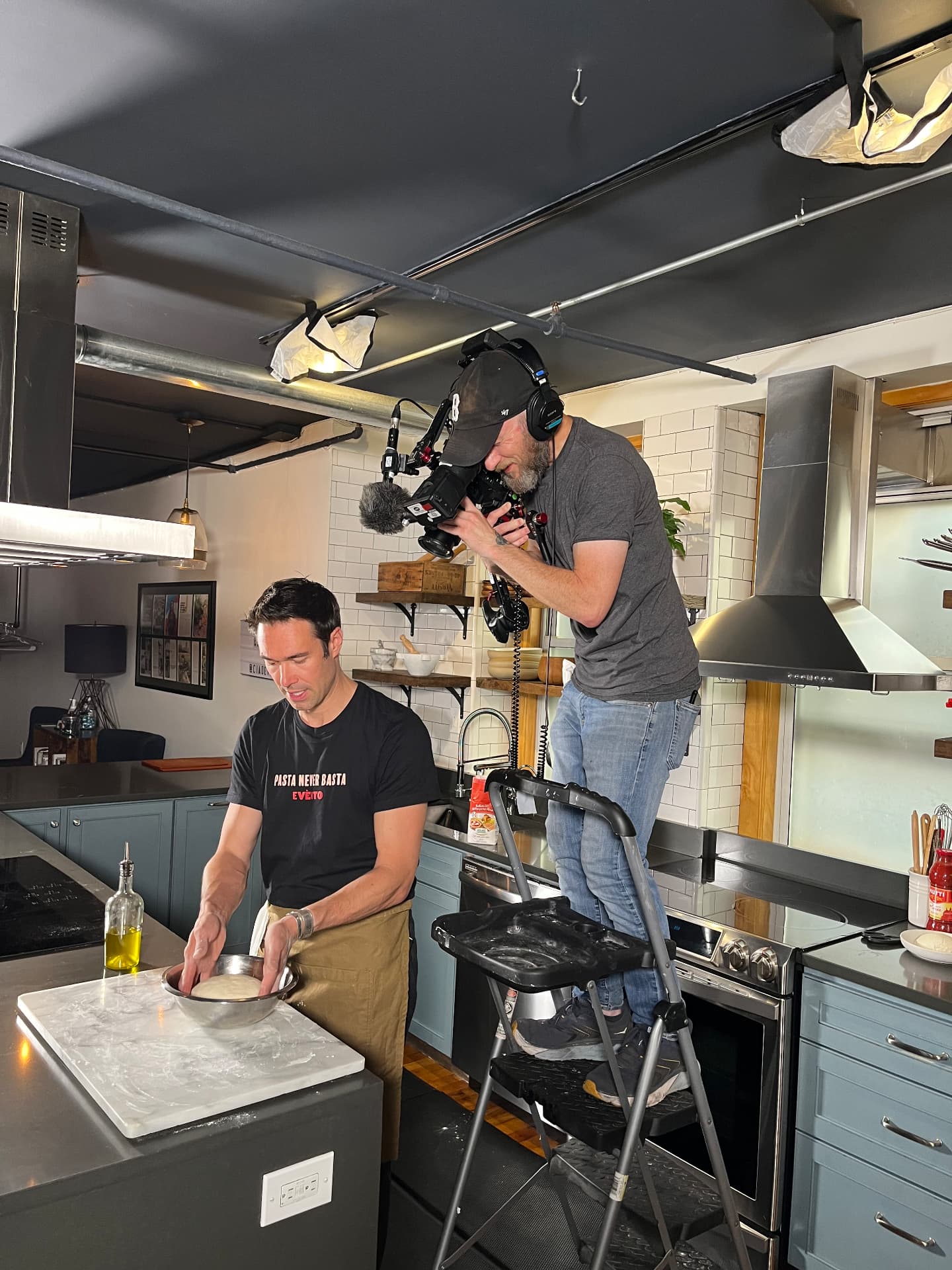 Gregory working dough while a camera operator films him in the studio.