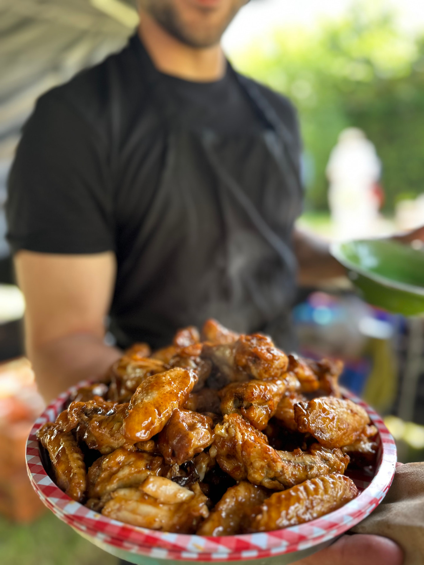 A generous plate of glazed chicken wings being served at an outdoor event.