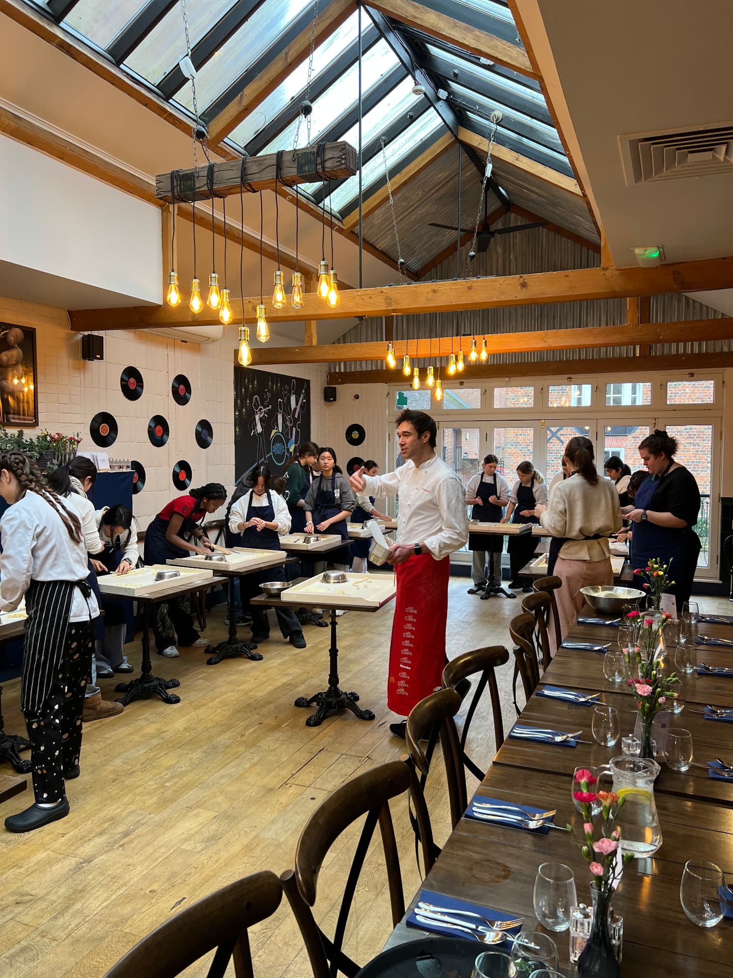 A large adult cookery class at work in a wood-beamed kitchen.