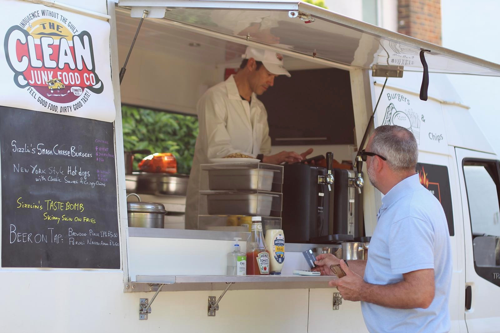The Clean Junk Food Co. truck serving guests through its open hatch.