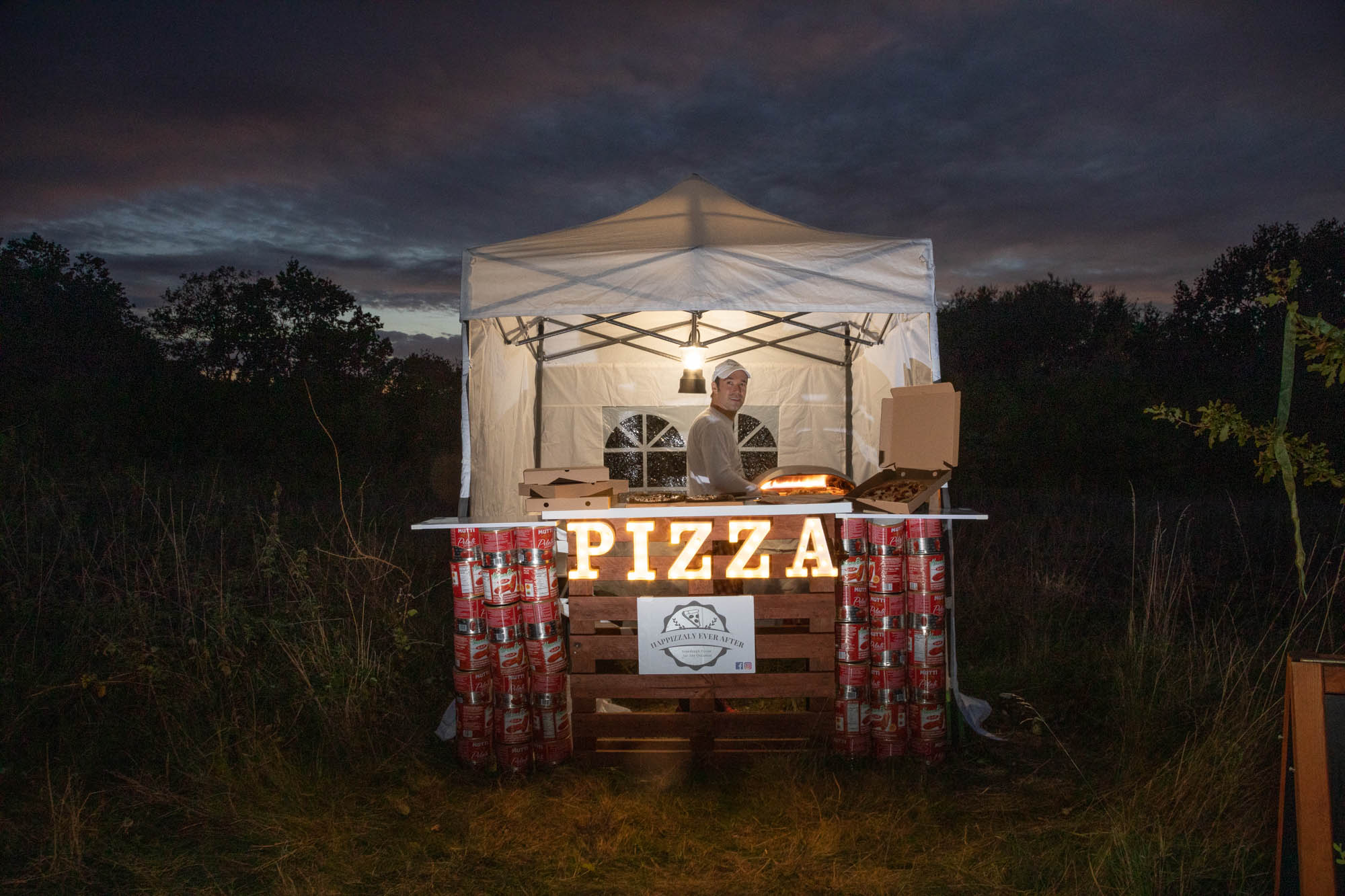 The Happizzaly Ever After pizza stand lit up at dusk.