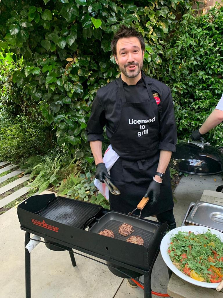 Gregory grilling burgers outdoors in a 'Licensed to grill' apron.