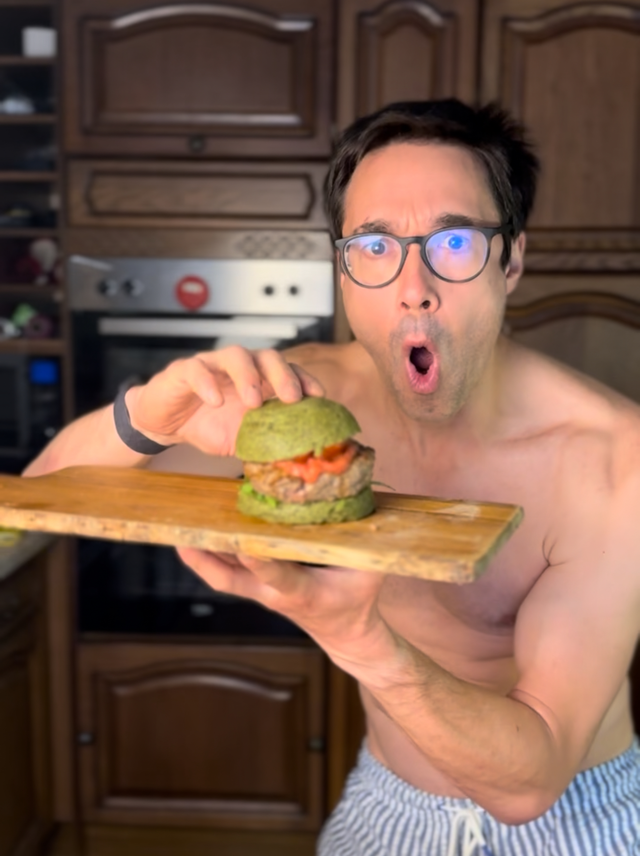 Gregory eating an enormous green burger in his own kitchen.