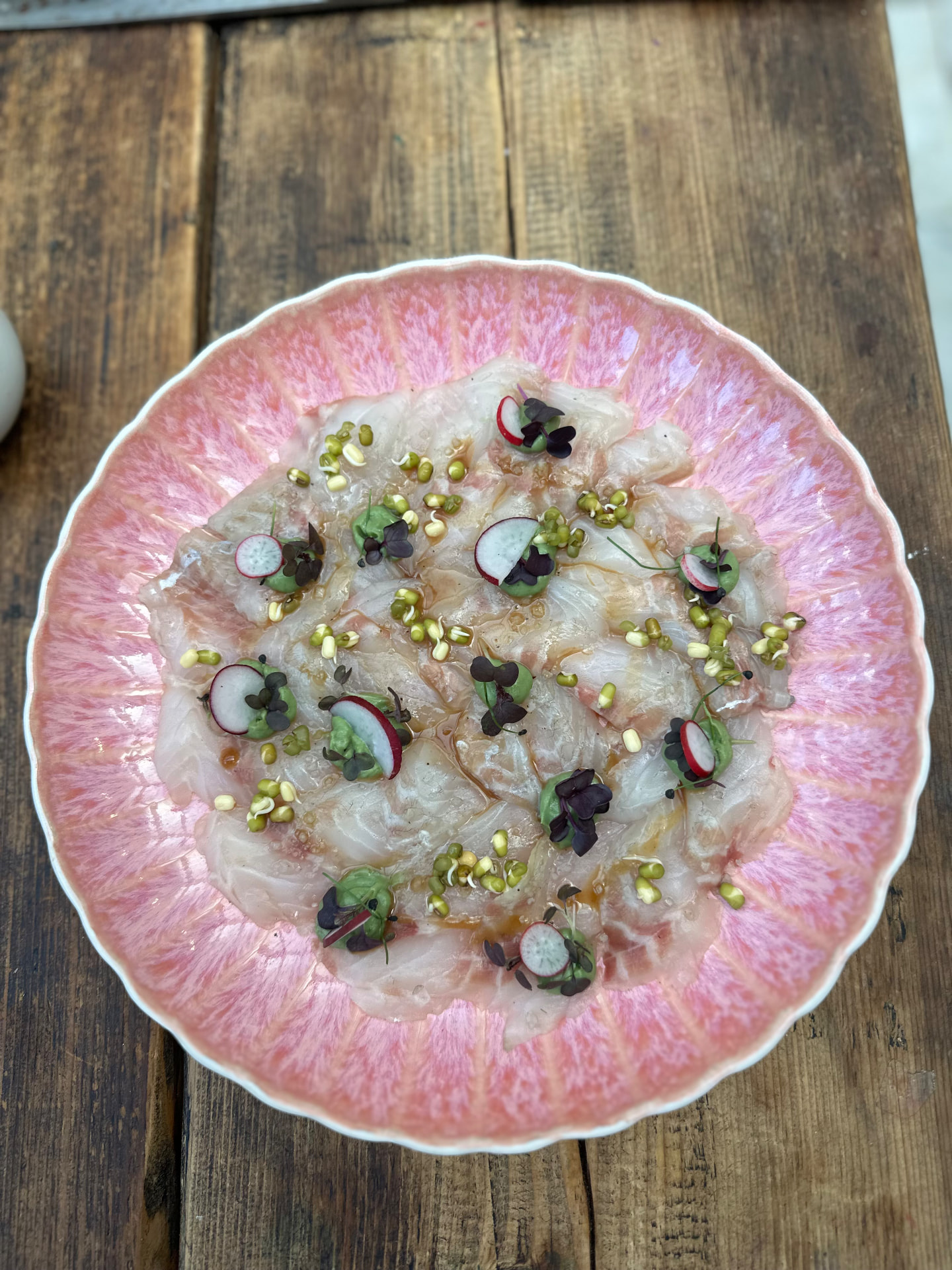 Translucent slices of raw fish with radish and herbs on a pink-rimmed plate.
